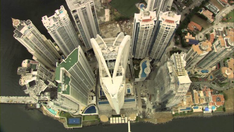 This is an aerial view of a dense urban area with numerous high-rise buildings, featuring a distinctive V-shaped skyscraper complex at the center.